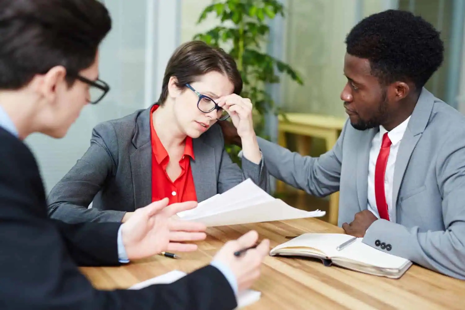 A business owner rests her head on her hand while two advisors review loan paperwork at a meeting table